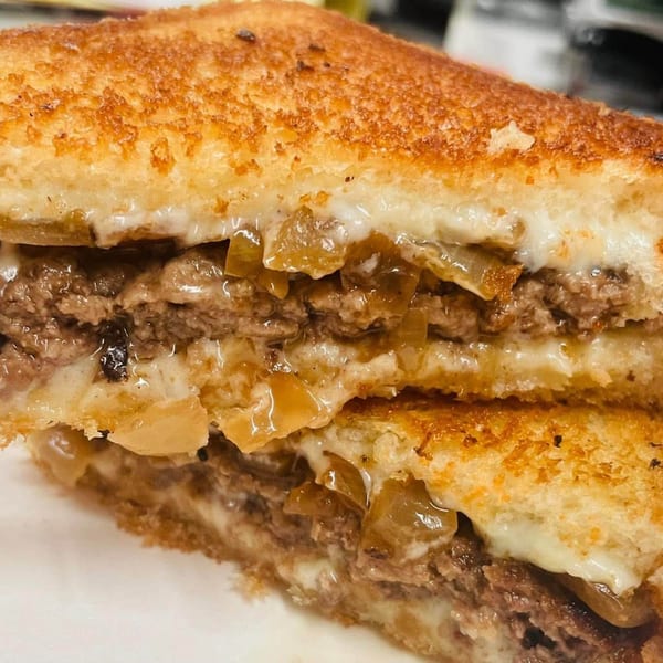 Close-up of a cut grilled cheese sandwich with melted cheese, ground beef, and caramelized onions.
