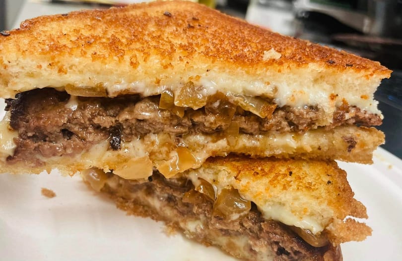 Close-up of a cut grilled cheese sandwich with melted cheese, ground beef, and caramelized onions.