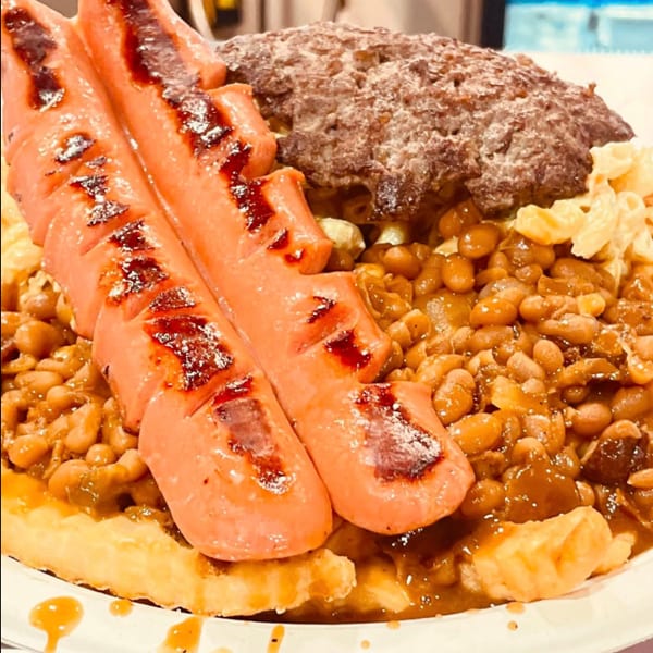A plate of grilled hot dogs, hamburger, baked beans, and macaroni salad over french fries.