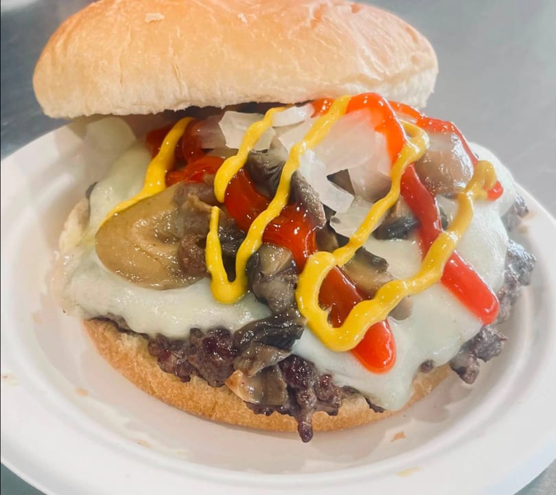 Cheesesteak sandwich with melted cheese, mushrooms, onions, ketchup, and mustard on a white plate.