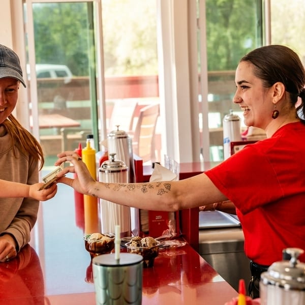 A young girl and her mother paying a smiling female cashier at a restaurant counter.