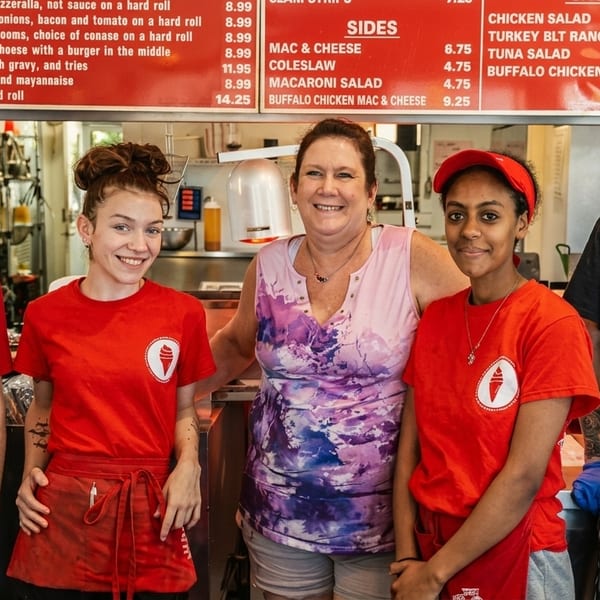 Five smiling restaurant staff members, three in red shirts, one in a patterned top, and one in a black shirt.