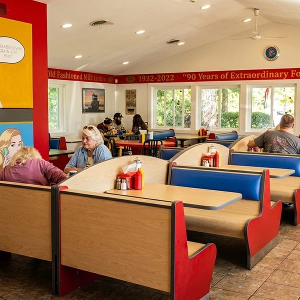 Diners seated in red and blue booths inside a brightly lit restaurant with large windows and pop art.