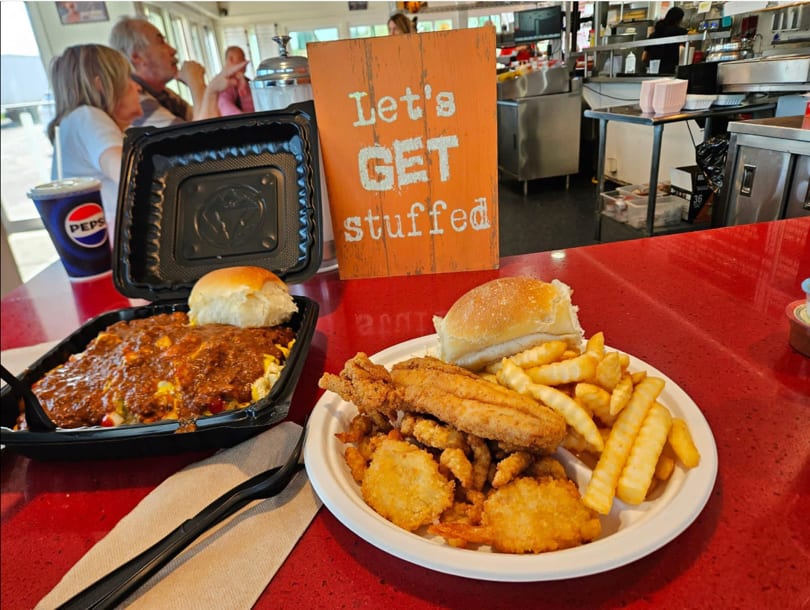 Two plates of food, one with chili and a bun, the other with fried fish, shrimp, and fries.